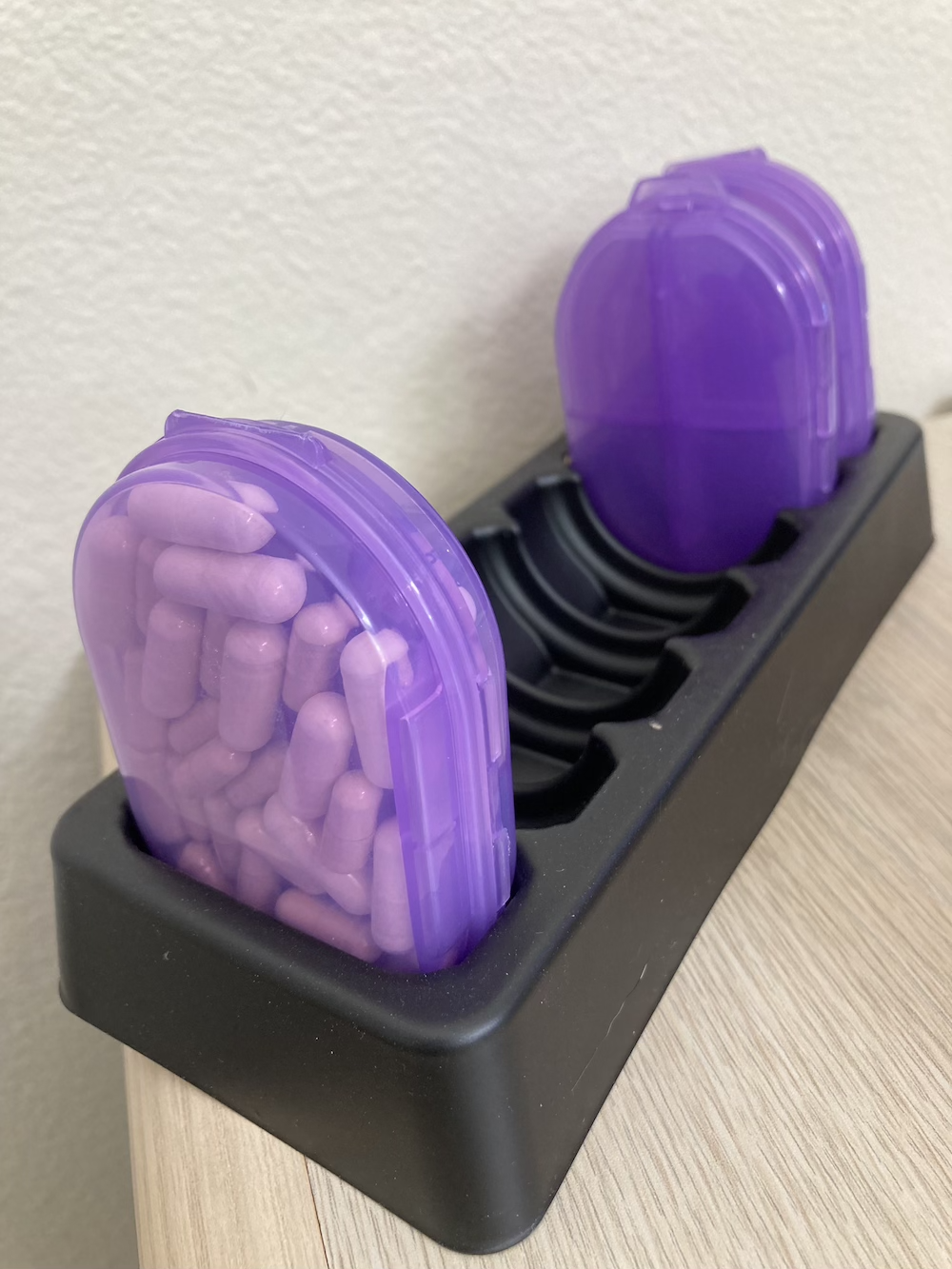 One purple multi-pill organizer filled with multiple types of pills, in a tray that holds 7 of these containers.