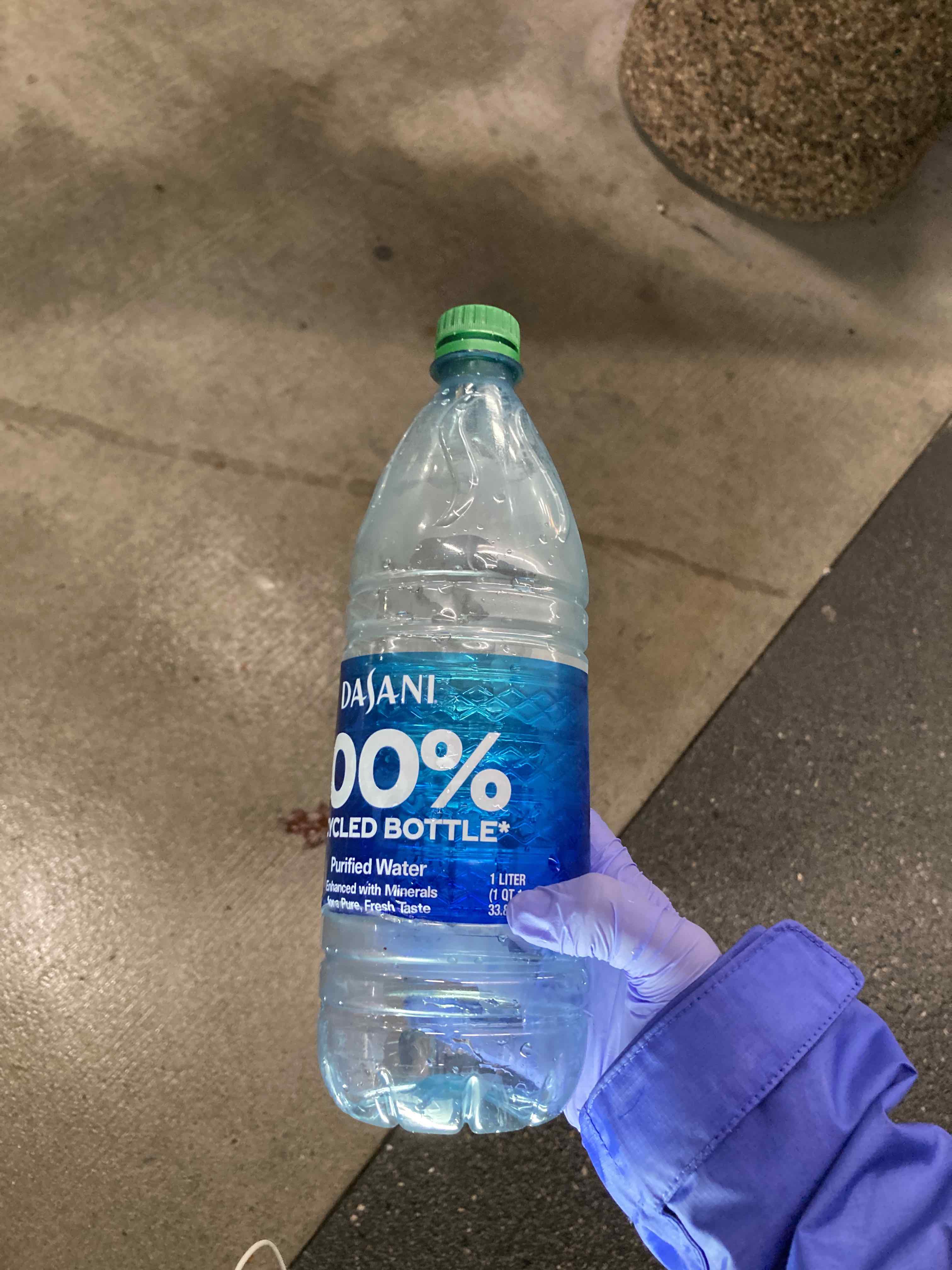 A 1-liter wattle bottle held in a hand covered with a blue nitrile gloves.